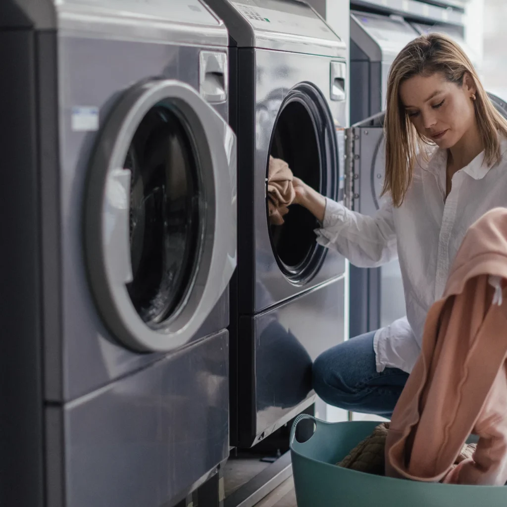 Woman loading clothes into a washing machine at a self-service laundromat