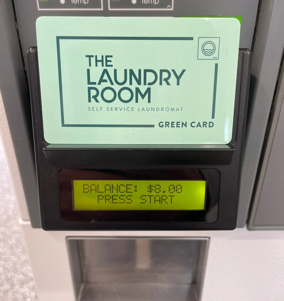 The Laundry Room Green Card in a machine card reader showing an $8.00 balance