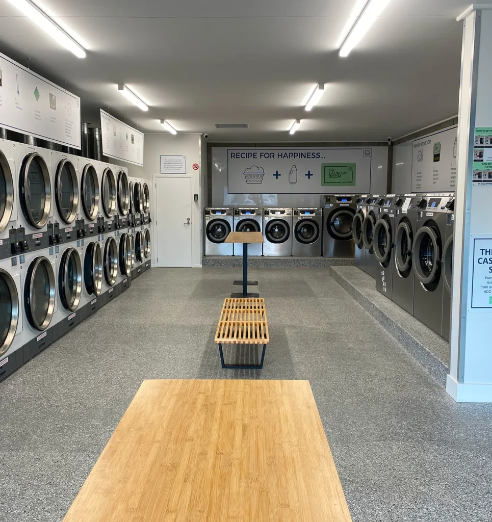 Long, bright laundromat with rows of washers, dryers and a bench seat