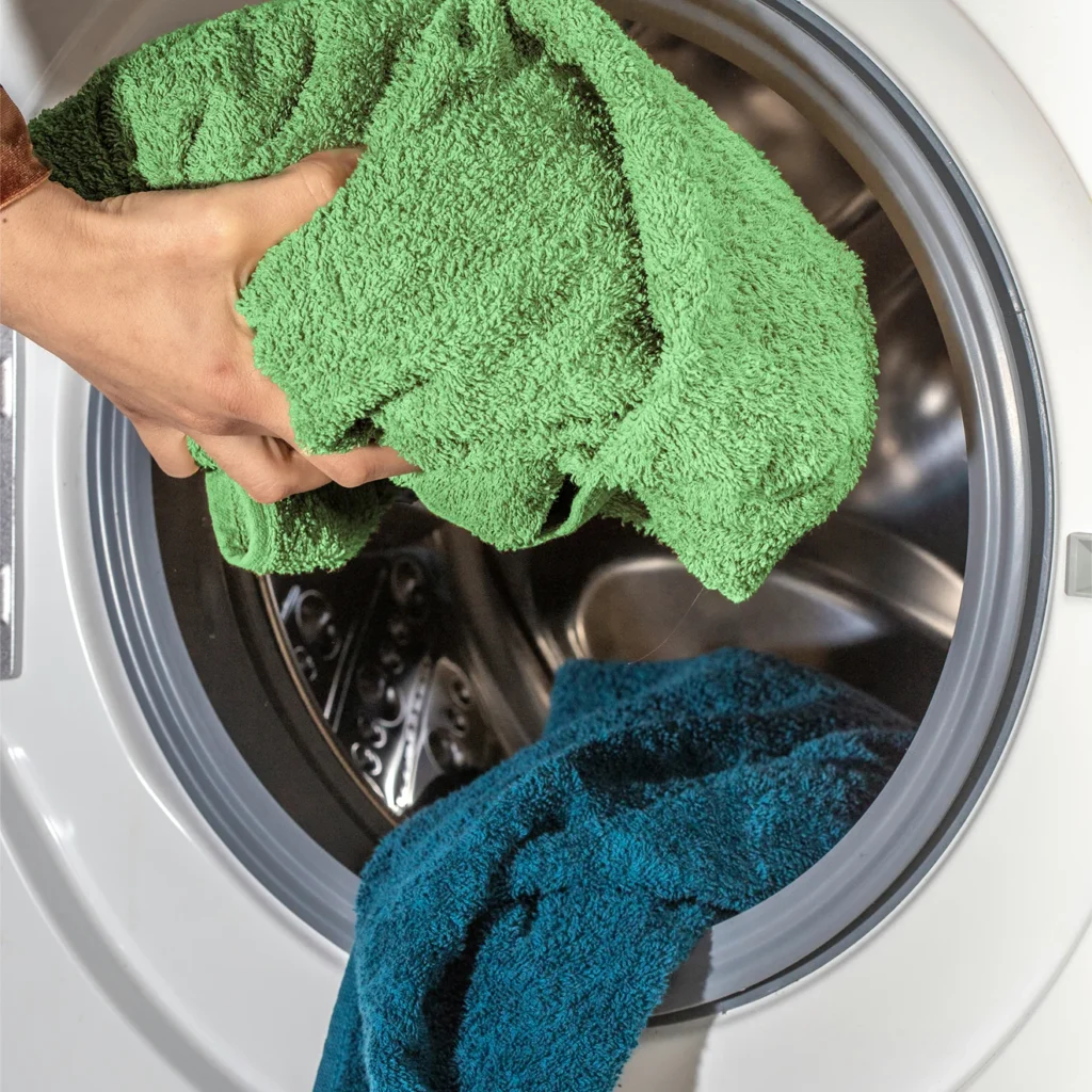 Green and teal towels going into a front-loading washing machine